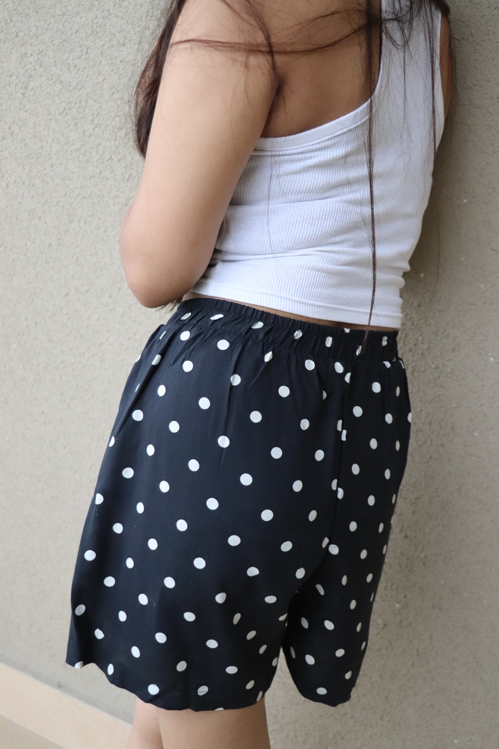 Side view of a woman wearing black polka dot viscose shorts with an elastic waistband and pockets.
