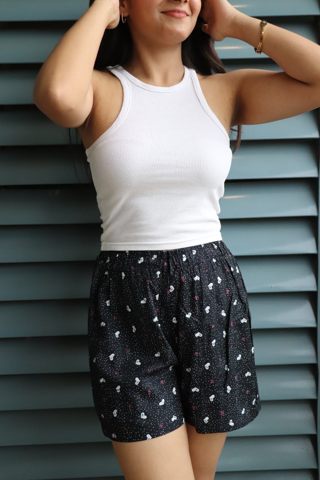 Woman in a white tank top wearing Mini Hearts viscose shorts with elastic waistband and pockets, perfect for lounging.