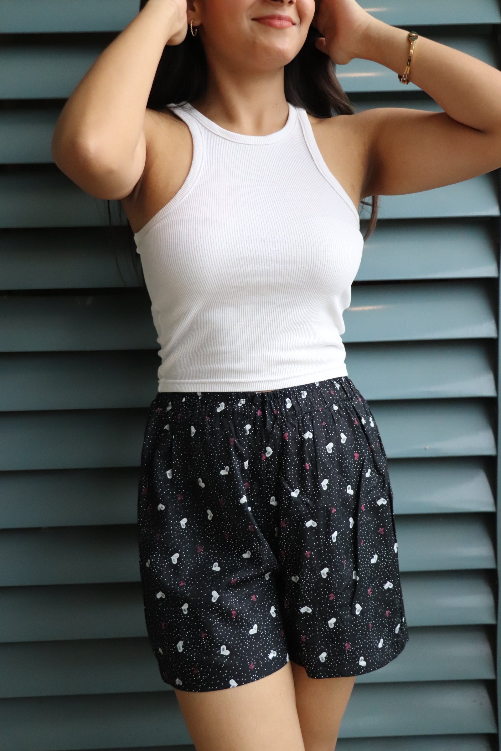 Woman in a white tank top wearing Mini Hearts viscose shorts with elastic waistband and pockets, perfect for lounging.
